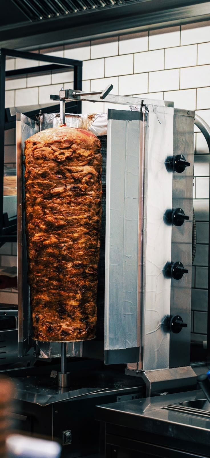 Dönerspieß am senkrechten Grill vor weißen Fliesen